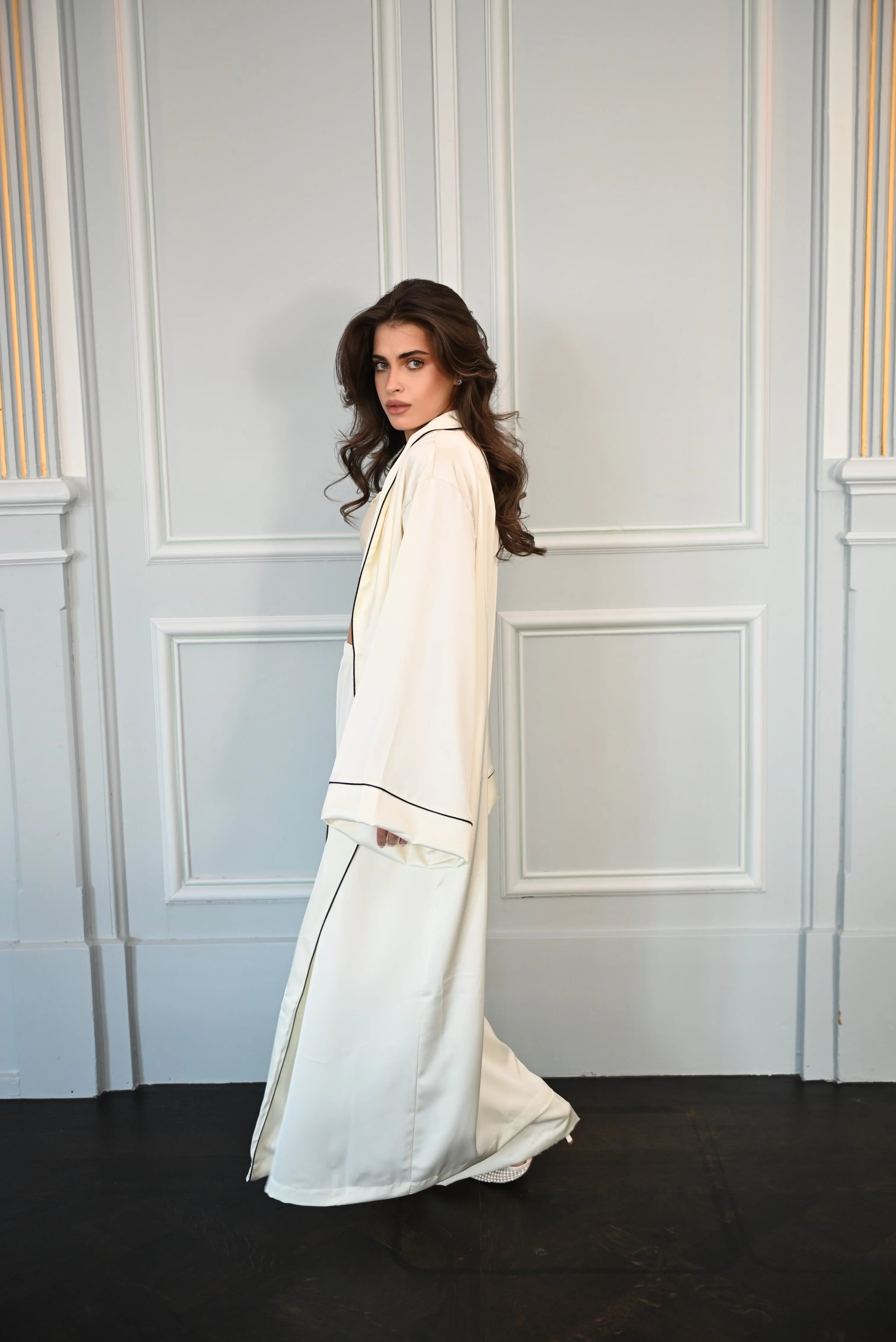 Woman in a Ivory white Kimano standing against a decorative wall.