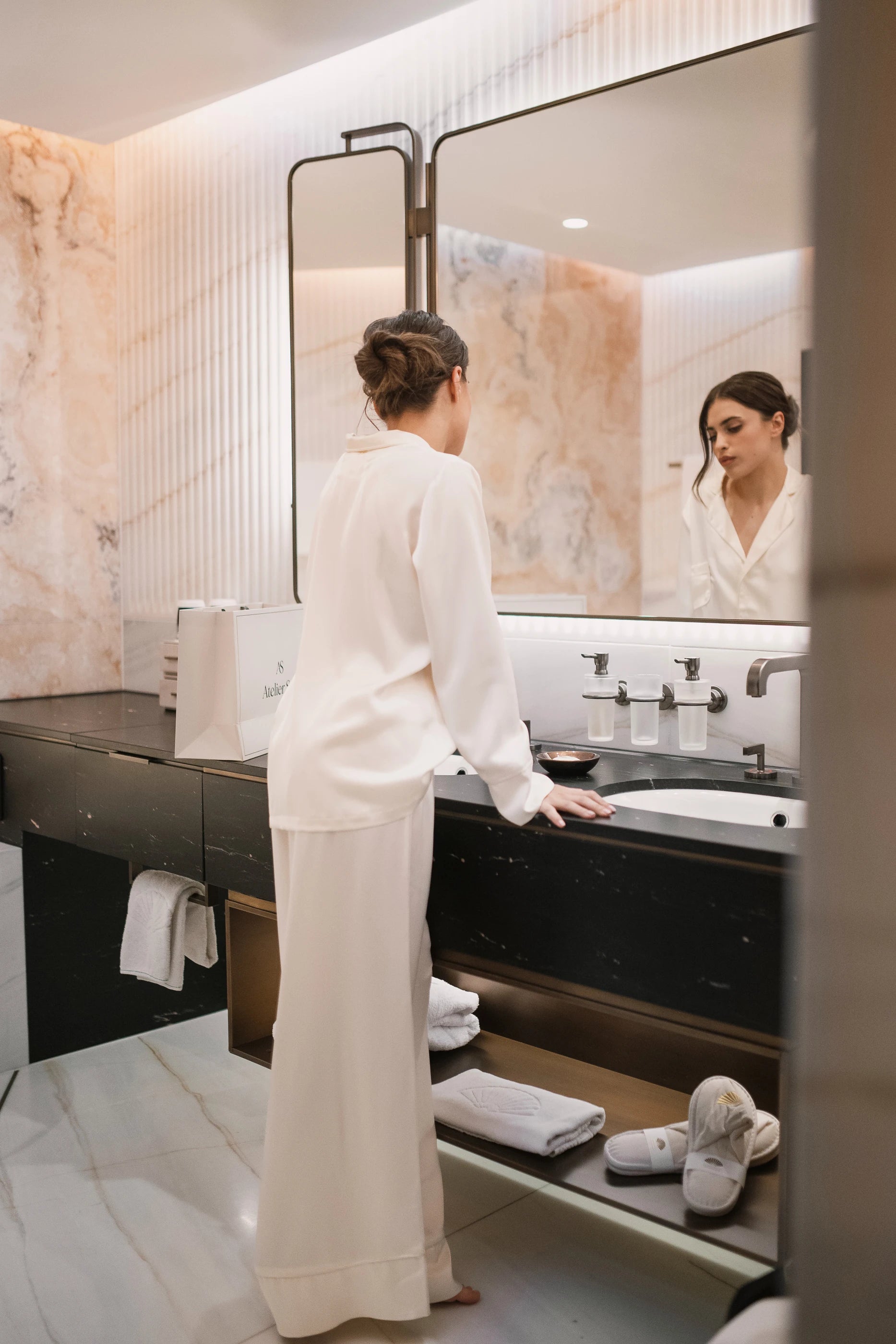 Woman in a ivory white outfit standing in a modern bathroom.