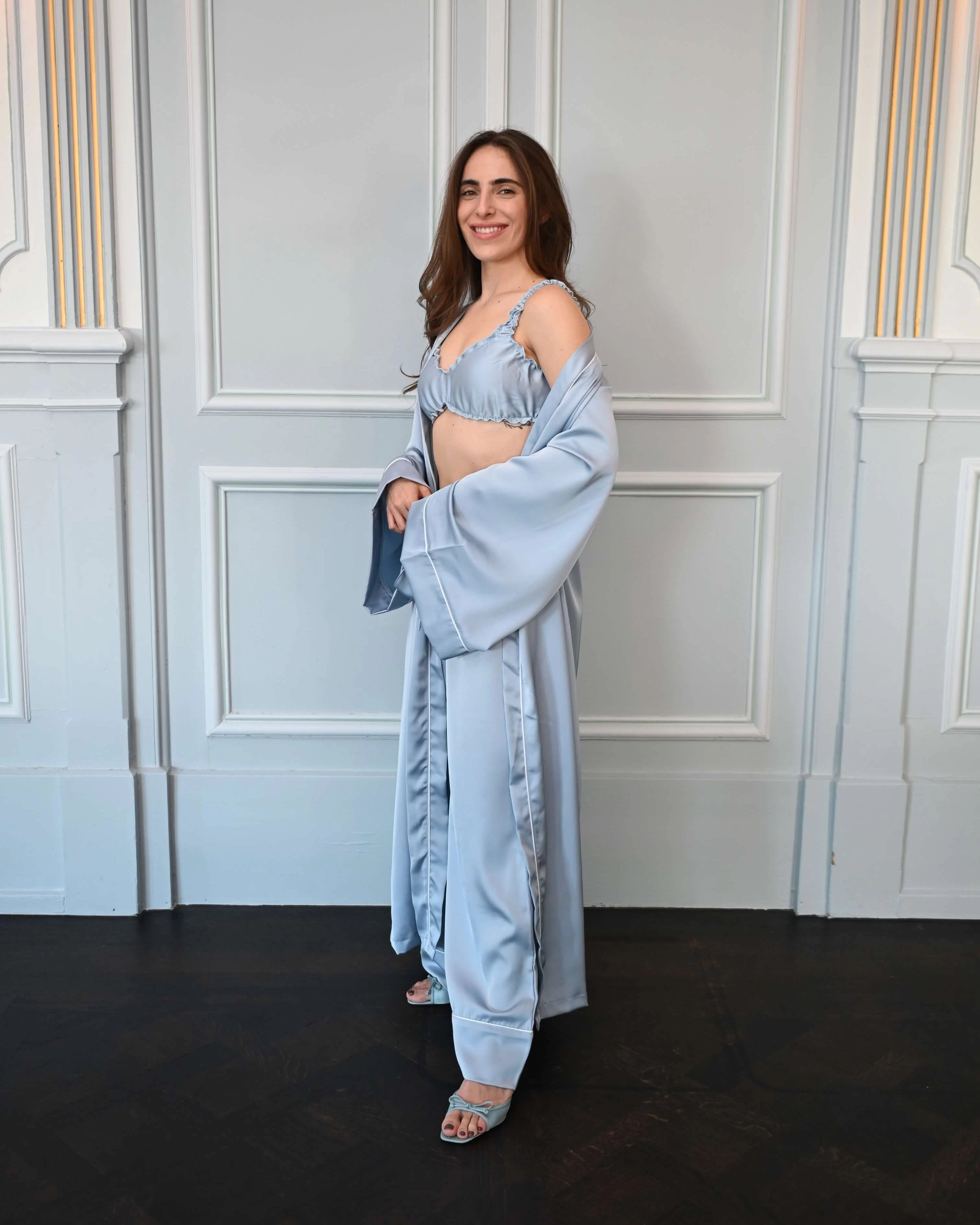 Woman in a light blue outfit standing against a white paneled wall.