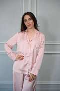 Woman wearing a pink satin pajama set against a gray background